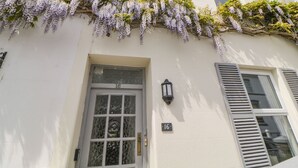 Un edificio con fachada blanca, una puerta con panel de vidrio y una ventana con contraventanas.