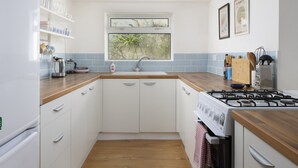 Cocina moderna con alacenas blancas, encimera de madera, estufa a gas y ventana con vistas a zonas verdes.