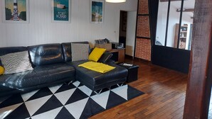 A modern living room with a black leather sofa, a black and white checkered rug, and wooden flooring. There are framed pictures on the wall and a hanging light fixture.