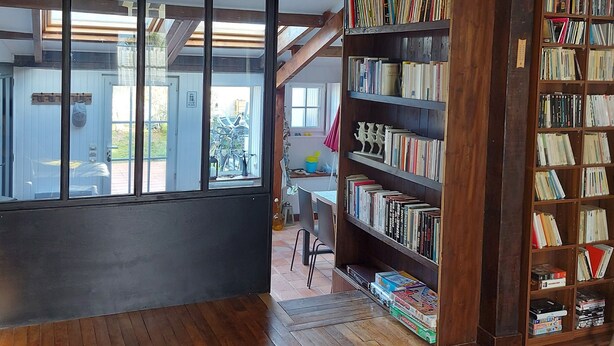 A spacious room with wooden floors, a large window, and a bookshelf filled with books.