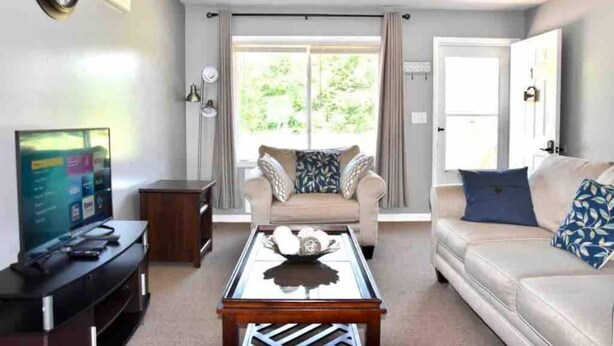 A living room with a sofa, a coffee table, a TV, and a sliding glass door leading to a balcony.