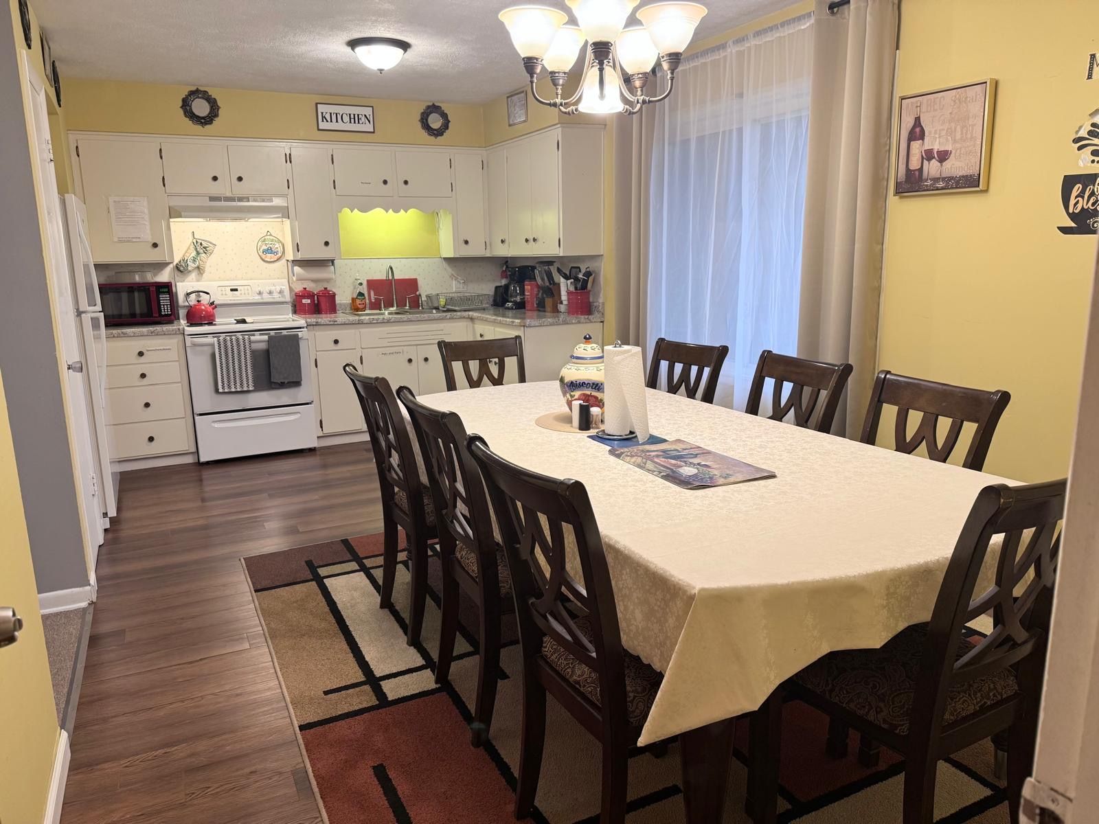 A dining area with a table, chairs, and a kitchen in the background.