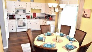 A dining area with a round table set for four, surrounded by wooden chairs. There is a kitchen area with white cabinets and a microwave.