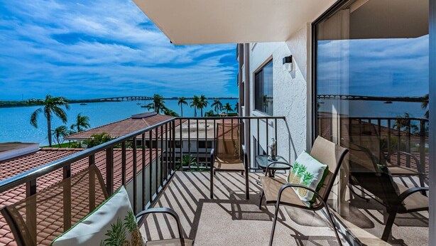 A balcony with a view of the sea and a bridge, furnished with chairs and a table. - Waterview 1BR condo with pool, hot tub, and balcony in St. Petersburg. (St Petersburg)