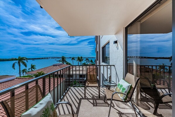 Un balcon avec vue sur la mer et un pont, aménagé avec des chaises et une table.