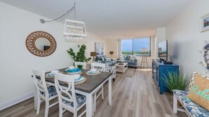 A modern living room with a dining area, a large window with a view, and a television on a stand. - Waterview 1BR condo with pool, hot tub, and balcony in St. Petersburg. (St Petersburg)