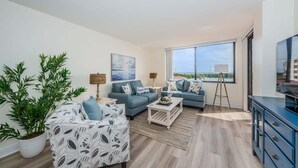 A modern living room with a sofa set, a coffee table, a TV, and a large window offering a view. - Waterview 1BR condo with pool, hot tub, and balcony in St. Petersburg. (St Petersburg)