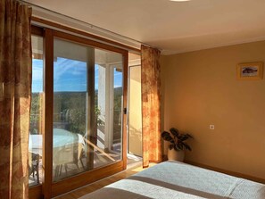 A bedroom with a sliding glass door to a balcony, a bed, a potted plant, and a framed picture on the wall.
