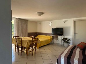 Una habitación con cama, televisor, mesa de comedor con sillas y una planta en maceta.