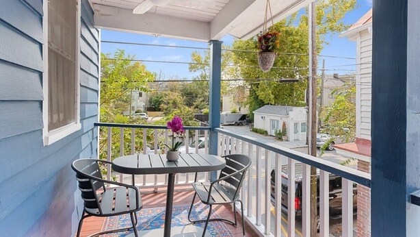 Un balcone coperto con tavolo e sedie, un vaso di fiori appeso e vista sul quartiere.
