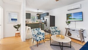 A modern kitchen with dark cabinets, a white refrigerator, and a microwave. There is a dining area with a round table and two patterned chairs. A ceiling fan is visible, and a TV is mounted on the wall. - Heart of Downtown - 1 Bedroom Suite w/ Parking! (Charleston)