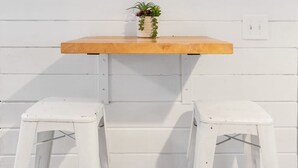 A white wall with a wooden shelf holding a small plant. Below the shelf, there are two white plastic stools. - Heart of Downtown - 1 Bedroom Suite w/ Parking! (Charleston)