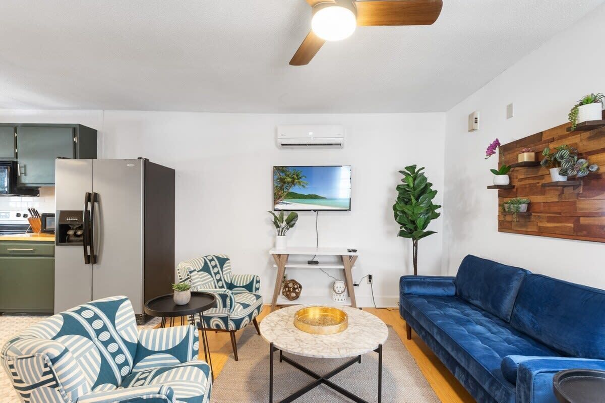 A modern living room with a blue sofa, patterned armchairs, a coffee table, and a ceiling fan.