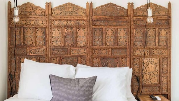A bed with white bedding and a single gray pillow, a wooden headboard with intricate carvings, and two hanging light bulbs. - Downtown Charmer! 3BD/3BA - 2 Blocks to King (Charleston)