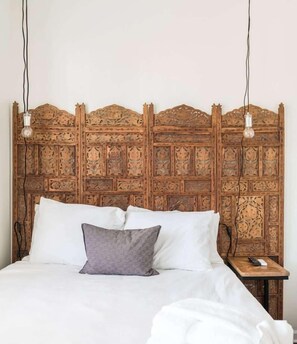 Un lit avec une literie blanche et un seul oreiller gris, une tête de lit en bois ornée de motifs complexes et deux ampoules suspendues.