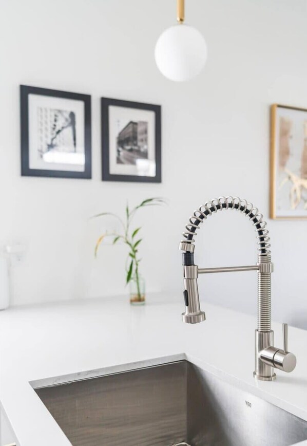 Una cocina moderna con un lavamanos de acero inoxidable, un grifo articulado y obras de arte enmarcadas en la pared.