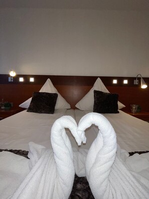 A hotel room with a neatly made bed, two pillows, a headboard, bedside lamps, and a heart-shaped towel decoration. - Griffin Hotel am Neumarkt (Cologne)