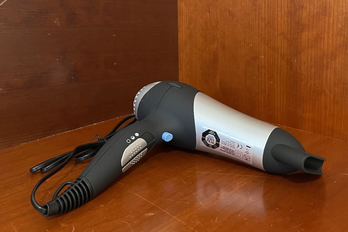 A hair dryer on a wooden floor next to a white wall and a wooden panel.