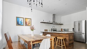 Una cocina moderna con una mesa de comedor de madera, sillas blancas, un refrigerador de acero inoxidable y un salpicadero de azulejos blancos.