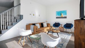 Una sala de estar moderna con una escalera, un sofá, dos sillones, una mesa de centro y un cuadro en la pared.