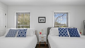 Habitación doble con dos camas, cada una con almohadillas estampadas, una mesita de noche pequeña con un jarrón y un cuadro en la pared.