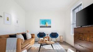 Una sala de estar moderna con un sofá marrón, dos sillones azules, una mesa de centro, un televisor y obras de arte en la pared.