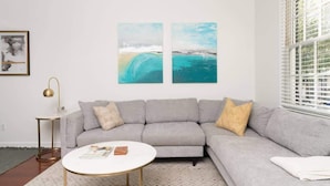 Ein modernes Wohnzimmer mit einem grauen Sofa, einem runden Couchtisch und zwei abstrakten Bildern an der Wand.