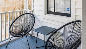 Eine überdachte Veranda mit zwei schwarzen Stuhlgestellen aus Draht und einem kleinen Tisch.