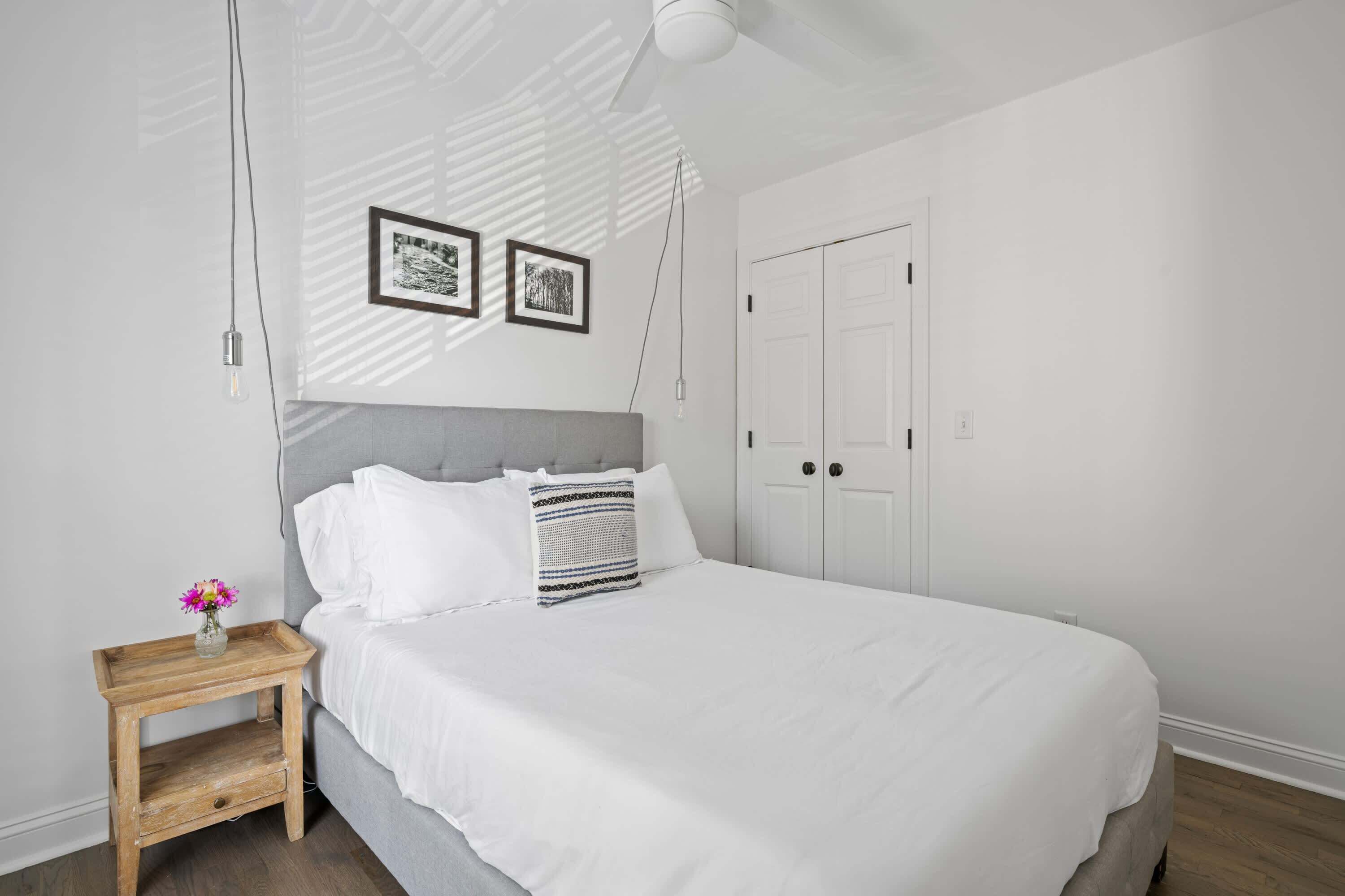 Un dormitorio con cama, mesita de noche con un florero y armario.