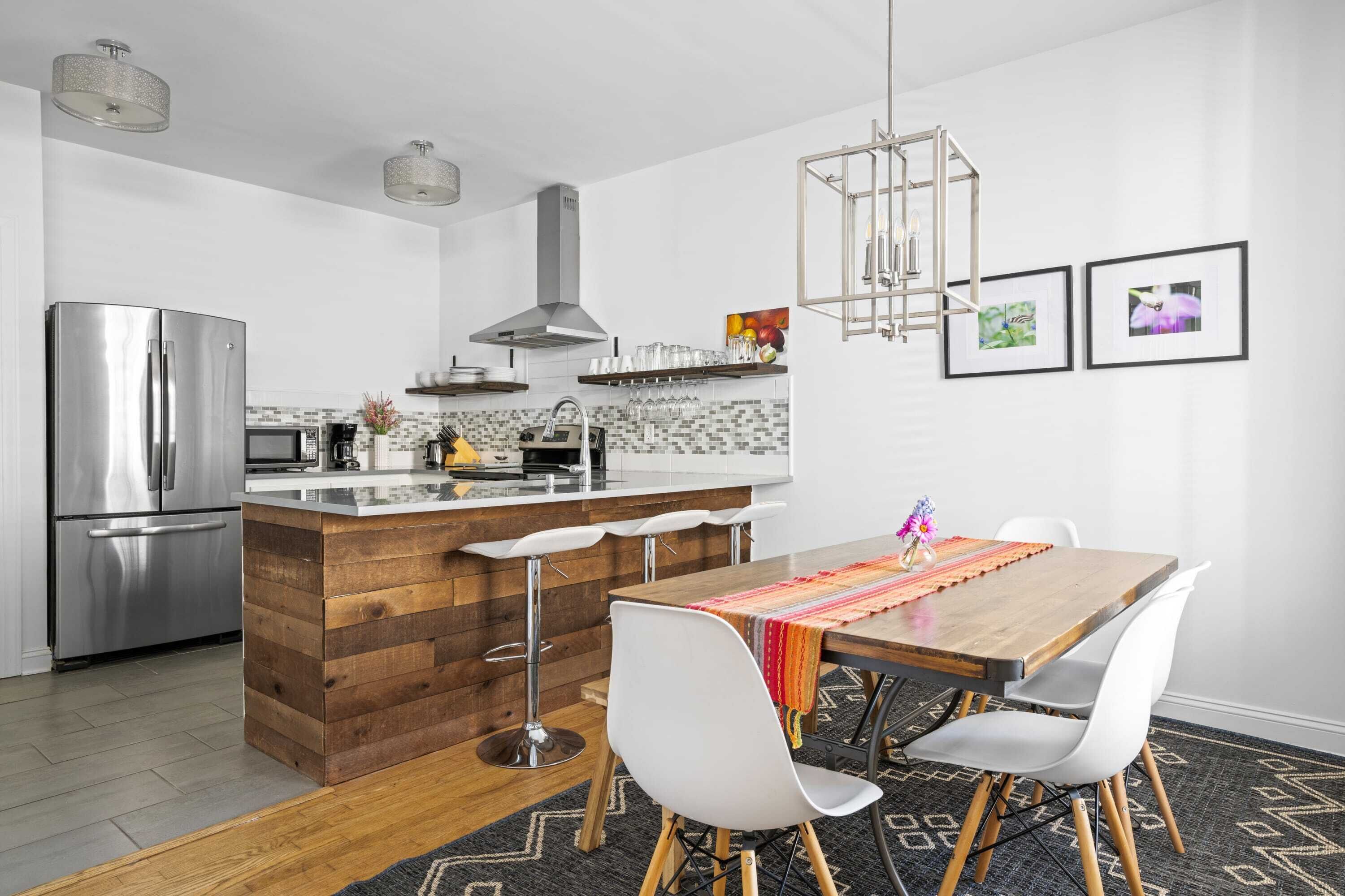 Una cocina moderna con una isla de madera, electrodomésticos de acero inoxidable y un comedor con sillas blancas y una mesa de madera.