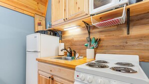 A compact kitchen with wooden cabinets, a white refrigerator, a stove, and a microwave. - Acorn Cottage | Adults-Only · Private Hot Tub · Secluded Hocking Hills Cabin (Logan)