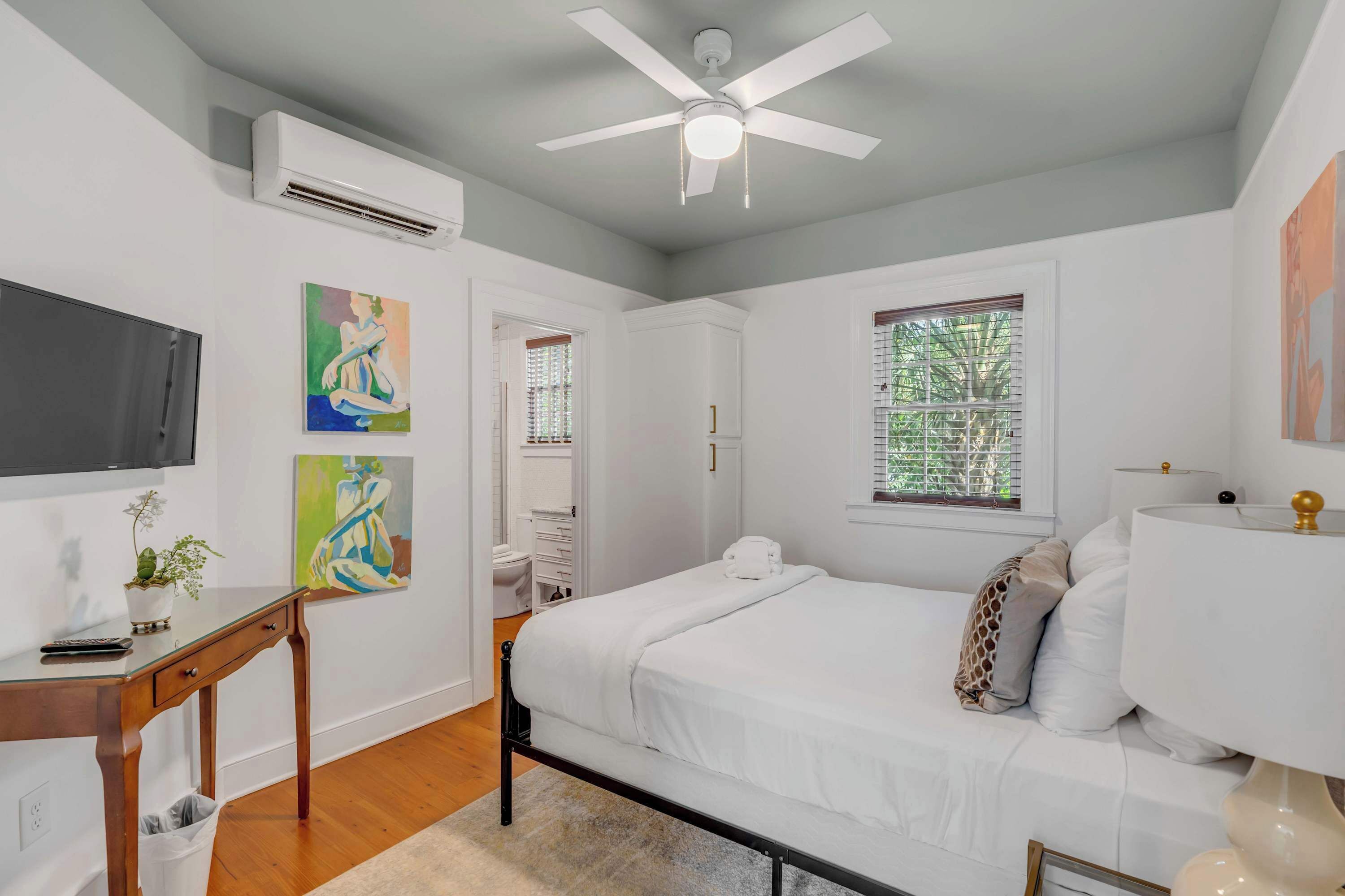 A bedroom with a bed, a desk, a TV, and artwork on the wall.