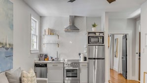 A modern kitchen with stainless steel appliances, a herringbone tile backsplash, and a view to the living area.