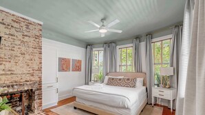 A bedroom with a brick wall, a bed, a ceiling fan, and a window with curtains.