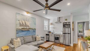 A modern kitchen with stainless steel appliances, a grey sofa, and a ceiling fan.