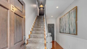 Un escalier avec des éléments en bois, un mur blanc orné de lambris et une œuvre d’art à la texture intéressante.