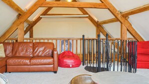 Un espace de vie de style loft avec un canapé en cuir marron, un fauteuil poire rouge, une table en métal et un plafond en bois avec des poutres apparentes.