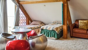 Une chambre avec deux lits, une chaise rouge et une chaise argentée, un canapé en cuir marron et une fenêtre à vitraux.