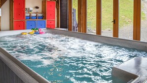 Un bain à remous avec des jouets, des meubles en bois et une vue sur une colline verdoyante.