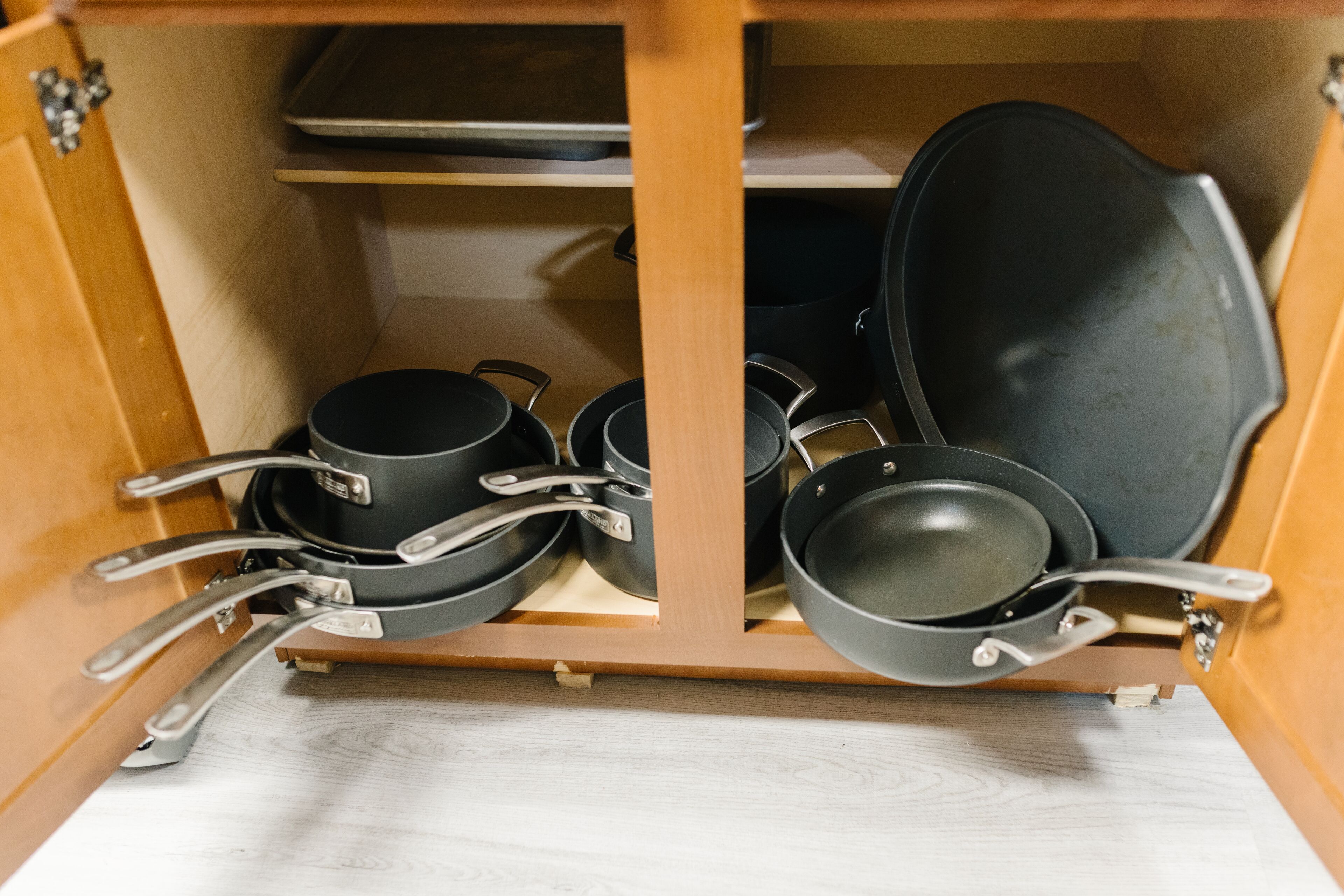 A kitchen cabinet with cookware including pots, pans, and a frying pan.