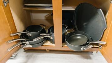 A kitchen cabinet with cookware including pots, pans, and a frying pan.