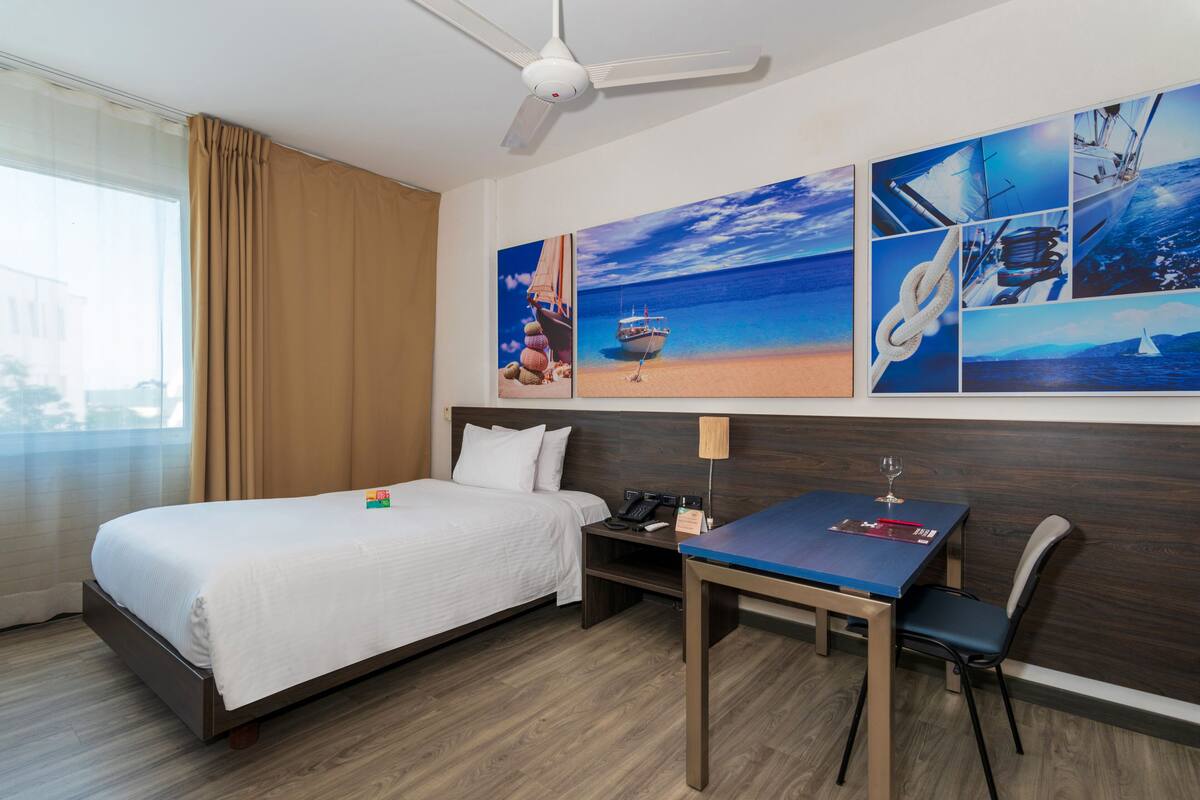 Une chambre d’hôtel avec un lit, un bureau, une chaise et un ventilateur de plafond.