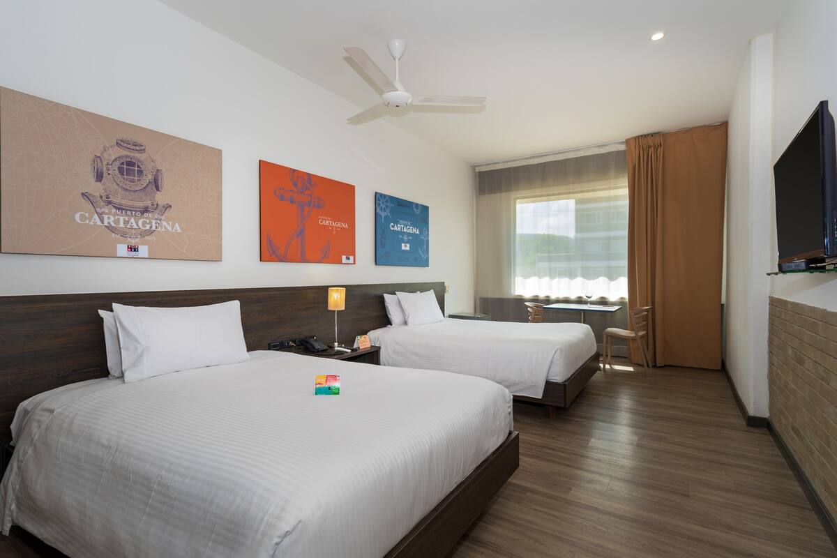 Une chambre d’hôtel avec deux lits, un ventilateur de plafond, une télévision et des œuvres d’art accrochées aux murs.