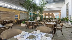 Un vaste espace intérieur aménagé pour les repas, avec des meubles en osier et des plantes en pot.