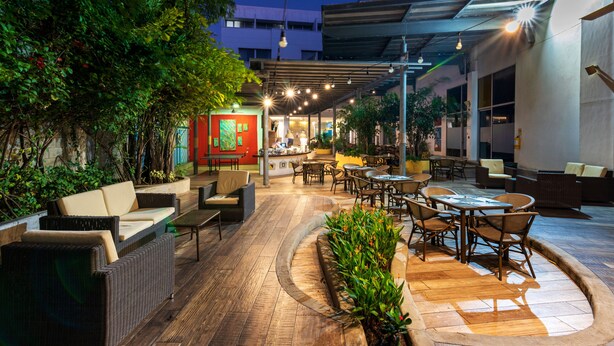 Un espace extérieur aménagé en terrasse, avec des meubles en osier, une table à manger centrale et des plantes en pot.