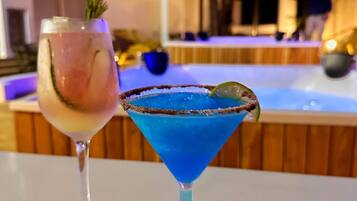 Dois cocktails numa mesa, com uma piscina e um deck de madeira ao fundo.