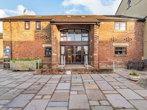 A brick building with a central entrance, stone paving, and outdoor seating.