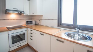 Una cocina con armarios blancos, un microondas, un horno, una ventana y un lavaplatos de acero inoxidable.
