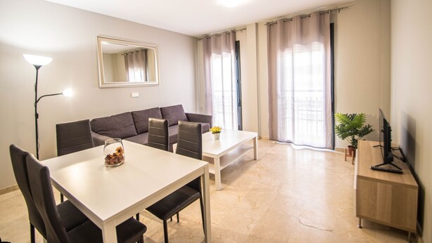 Una sala de estar moderna con un sofá, mesa de comedor, sillas, televisor y lámpara.