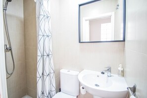 A bathroom with a shower, toilet, sink, and mirror.